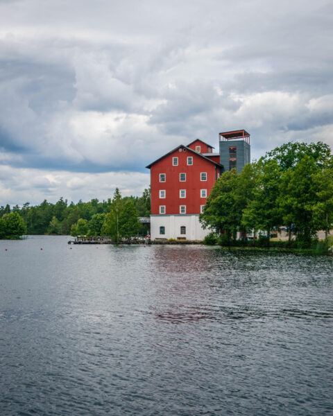 Stora röda silolbyggnaden Upperud 9:9 vid vattnet i Dalsland, omgiven av gröna träd under dramatisk molnhimmel