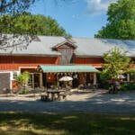 Café Allé vid Baldersnäs i Dalsland, ett sommarcafé inrymt i en faluröd lada med uteservering, markiser och parasoll en solig dag.