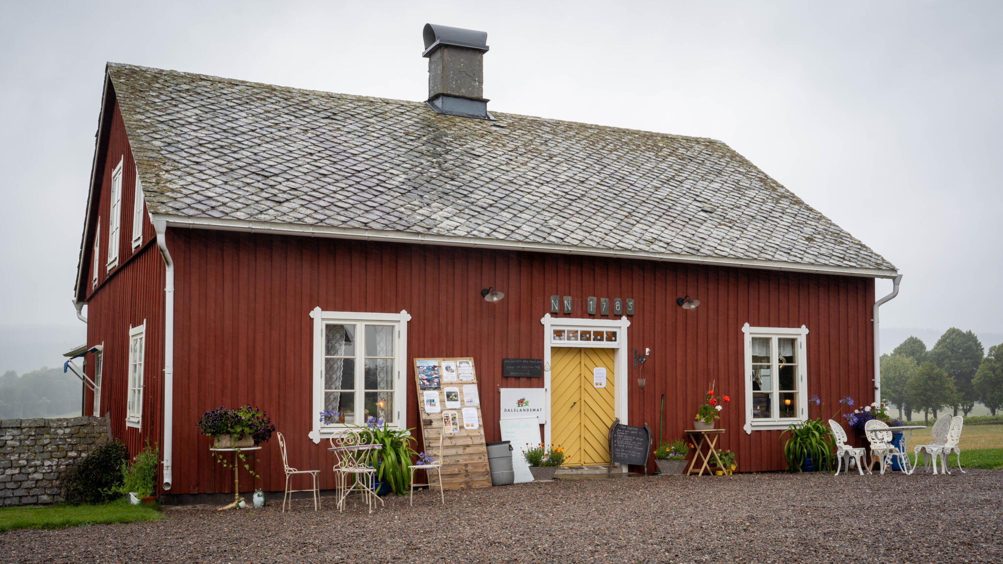 Faluröd sidobyggnad med gul dörr och uteservering vid Ekholmen Café & Gårdsbutik, ett gammalt säteri vid Kroppefjäll i Dalsland
