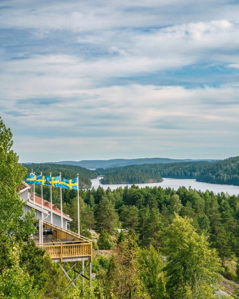 Kaffestugan på Majberget med svenska flaggor och utsikt över sjön och skogarna kring Bengtsfors i Dalsland