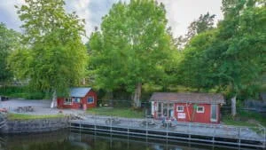 Röda små cafébyggnader vid slussen i Köpmannebro längs Dalslands kanal, omgivna av grönskande lövträd en sommardag