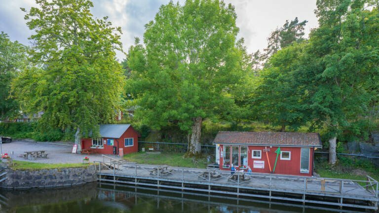Röda små cafébyggnader vid slussen i Köpmannebro längs Dalslands kanal, omgivna av grönskande lövträd en sommardag