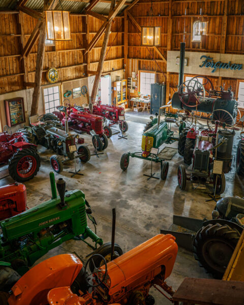 Samling av veterantraktorer i en rymlig lada på Odalmannens museum i Gamla Linköping, med John Deere, Ferguson och Farmall bland övriga maskiner.