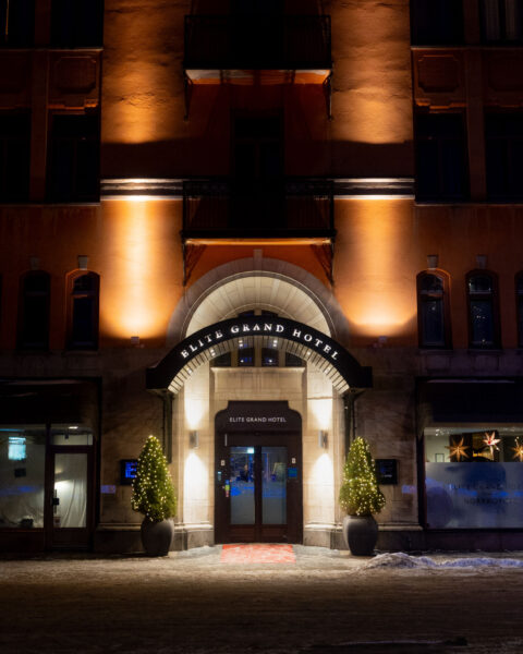 Upplyst entré till Elite Grand Hotel i Norrköping en vinterkvll, med julgranar med belysning och röd matta vid ingången.