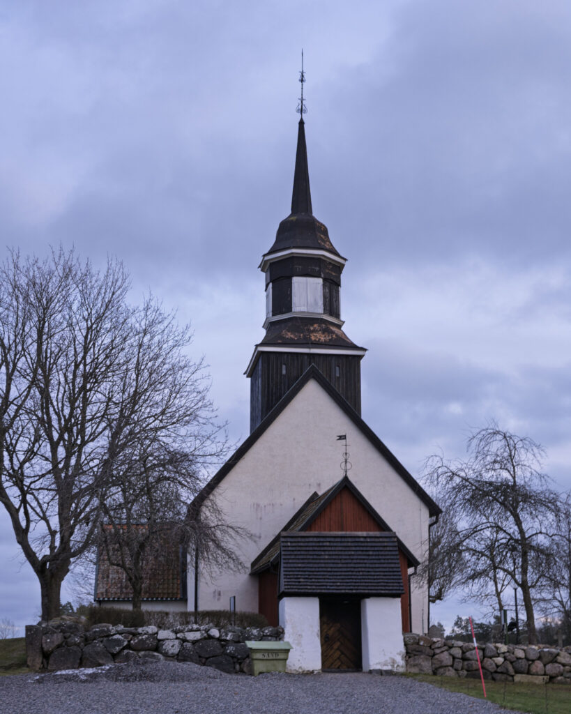 Lillkyrka kyrka i Östergötland, en vitputsad medeltida kyrka med mörkt trätorn och spira, omgiven av stenmur och kala träd en mulen vinterdag.