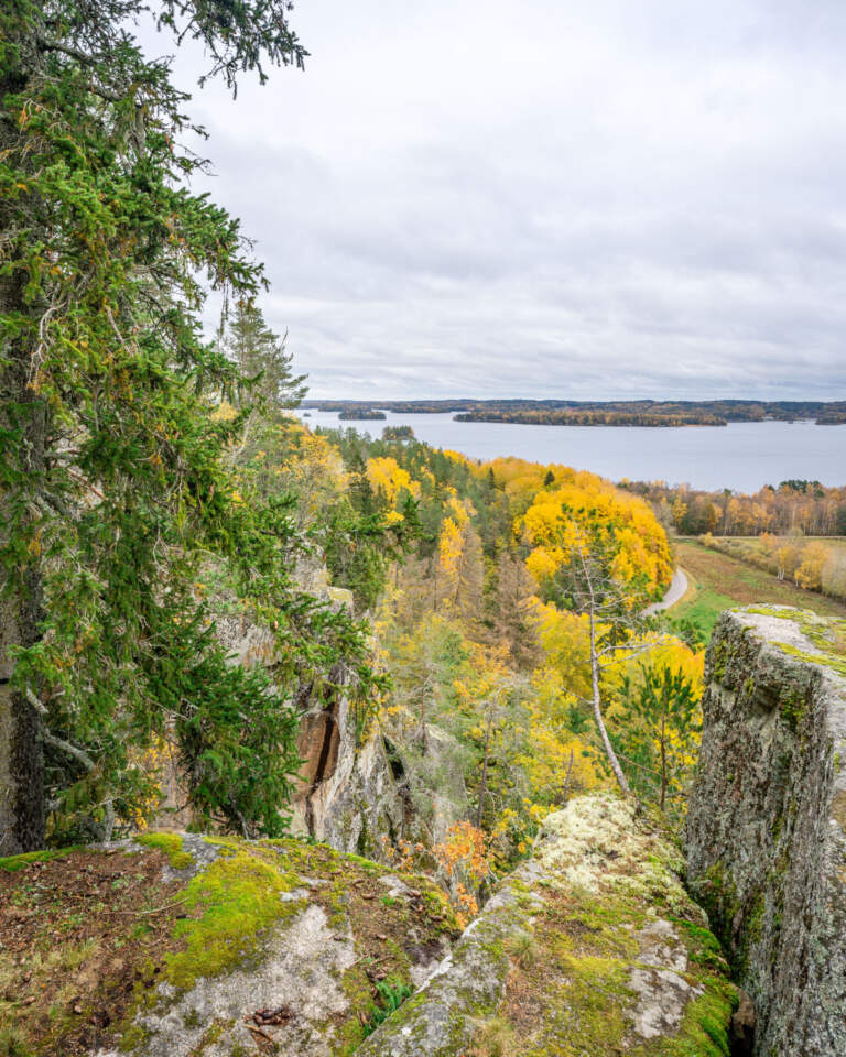 Utsikt från Klevberget i höstfärger med mosstäckta klippor, gulnande lövträd, granar och Ärlången i bakgrunden, Kinda kommun