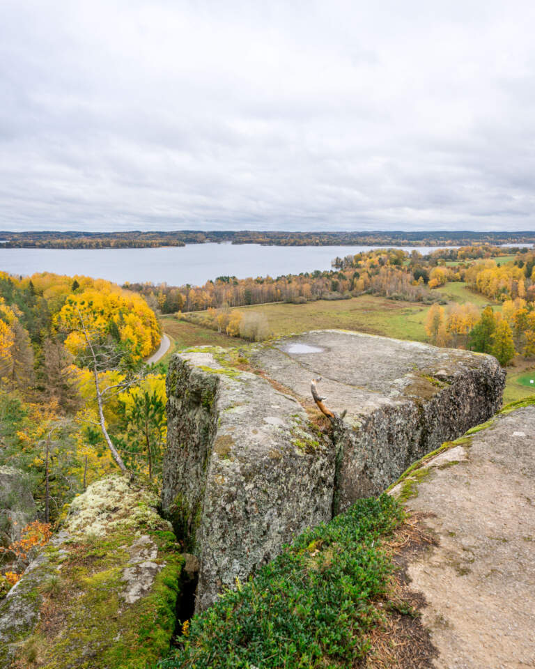 Utsikt från Klevberget i Kinda över höstfärgat landskap med sjön Ämmern, gröna ängar och gula lövträd en mulen dag.