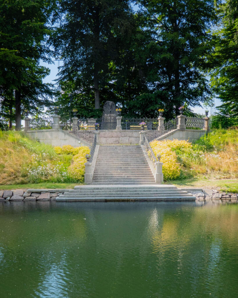 Baltzar von Platens grav vid Göta kanal i Motala, med stentrappa från vattnet upp till monumentet omgivet av grönska och höga träd