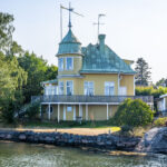 Gult sekelskifteshus med torn och grönpatinerat koppartak vid vattnet i Arkösund, Östergötland
