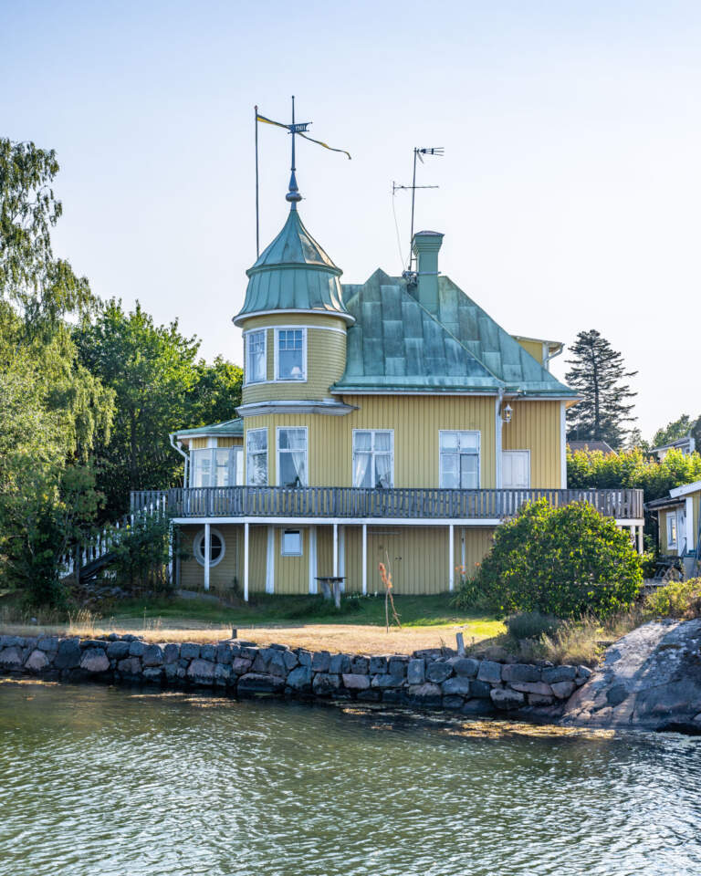 Gult sekelskifteshus med torn och grönpatinerat koppartak vid vattnet i Arkösund, Östergötland