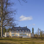 Villa Fridhem i Kolmården, ett elegant herrgårdsliknande boutiquehotell omgivet av grön parkmark och svensk flagga en solig vårdag