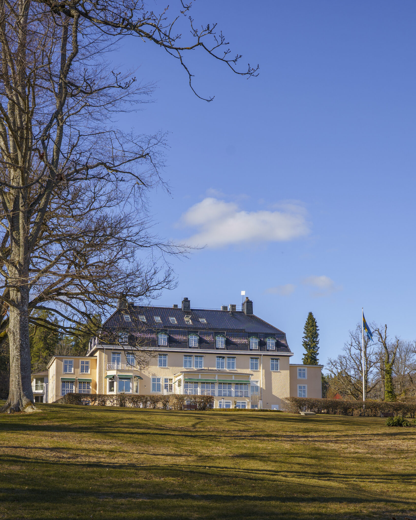 Villa Fridhem i Kolmården, ett elegant herrgårdsliknande boutiquehotell omgivet av grön parkmark och svensk flagga en solig vårdag
