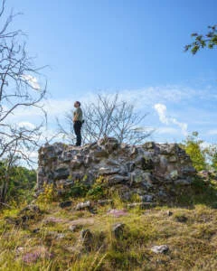 Person står på ruinen av Uttersbergs kastal i Krokek, en medeltida borgruin omgiven av ljung och buskar under blå himmel.