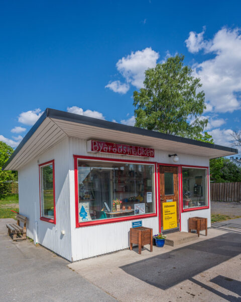 Byarådsknacken i Rejmyre, en liten vit kioskbyggnad med röda fönsterkarmar och skylt, omgiven av grönska en solig sommardag.