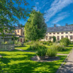 Grönskande Örtagården i Söderköping med grusgång, parkbänkar, blommande rabatter och historiska byggnader en solig sommardag