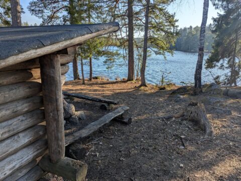 Vindskydd i timmer vid Övre Glotterns strand med sittbänk, omgivet av tallskog i solljus, Norrköpings kommun