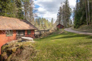 Rödfärgade byggnader vid Ingvastebo såg och kvarn omgivna av skog, med en slingrig grusväg och grön gräsmatta i förgrunden.