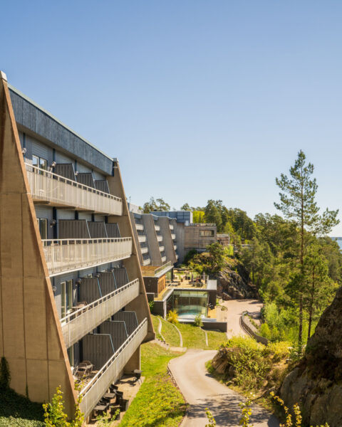 Vildmarkshotellet i Kolmården med balkongklädda fasader inbyggda i klipplandskap omgivet av tallskog och blå himmel.