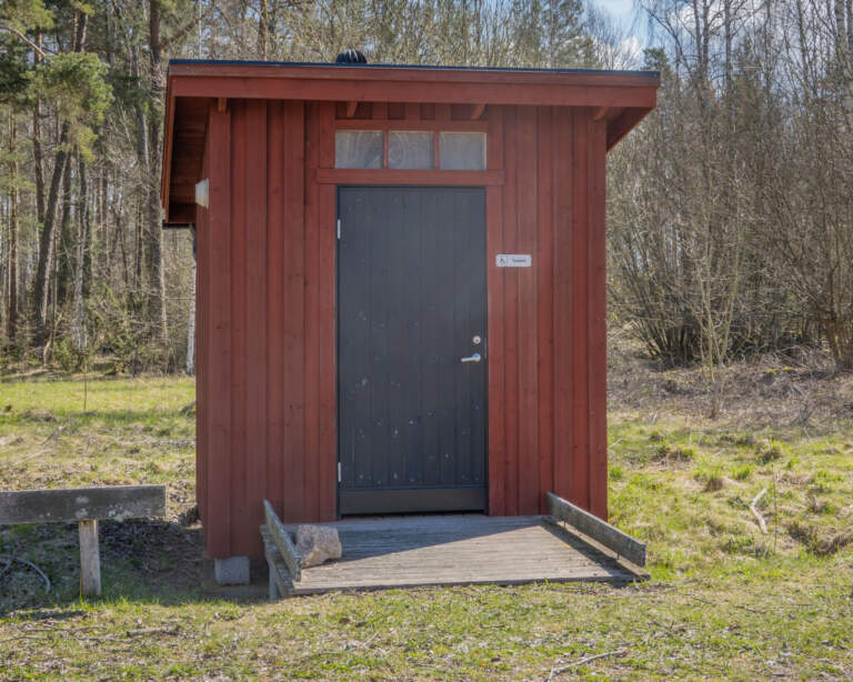 Faluröd torrtoa med mörk dörr och handikappanpassad ramp vid Svälinge vandringsled nära Tåkern, Östergötland