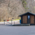 Toalettbyggnad i trä vid parkeringen på Omberg, Östergötland, omgiven av lövskog i tidig vår.