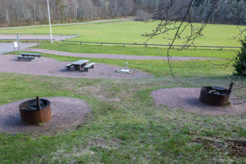 Grillplatser med eldringarna och picknickbord vid Stocklycke på Omberg, med grön gräsmatta och skog i bakgrunden.