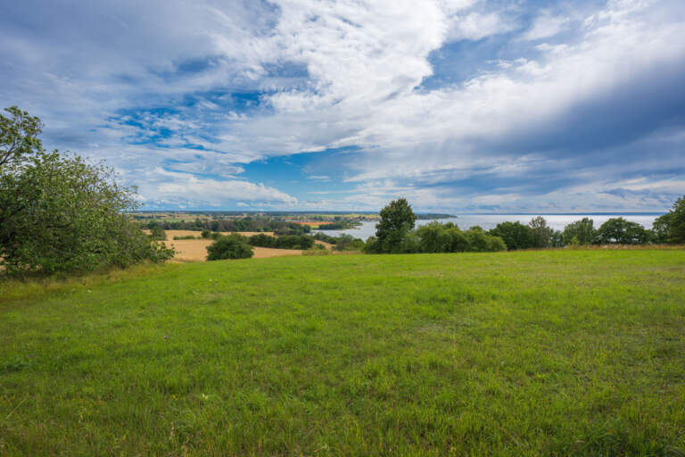 Vidsträckt utsikt från Sverkersgårdens rastplats på Omberg med gröna ängar, odlingslandskap och Vättern i bakgrunden