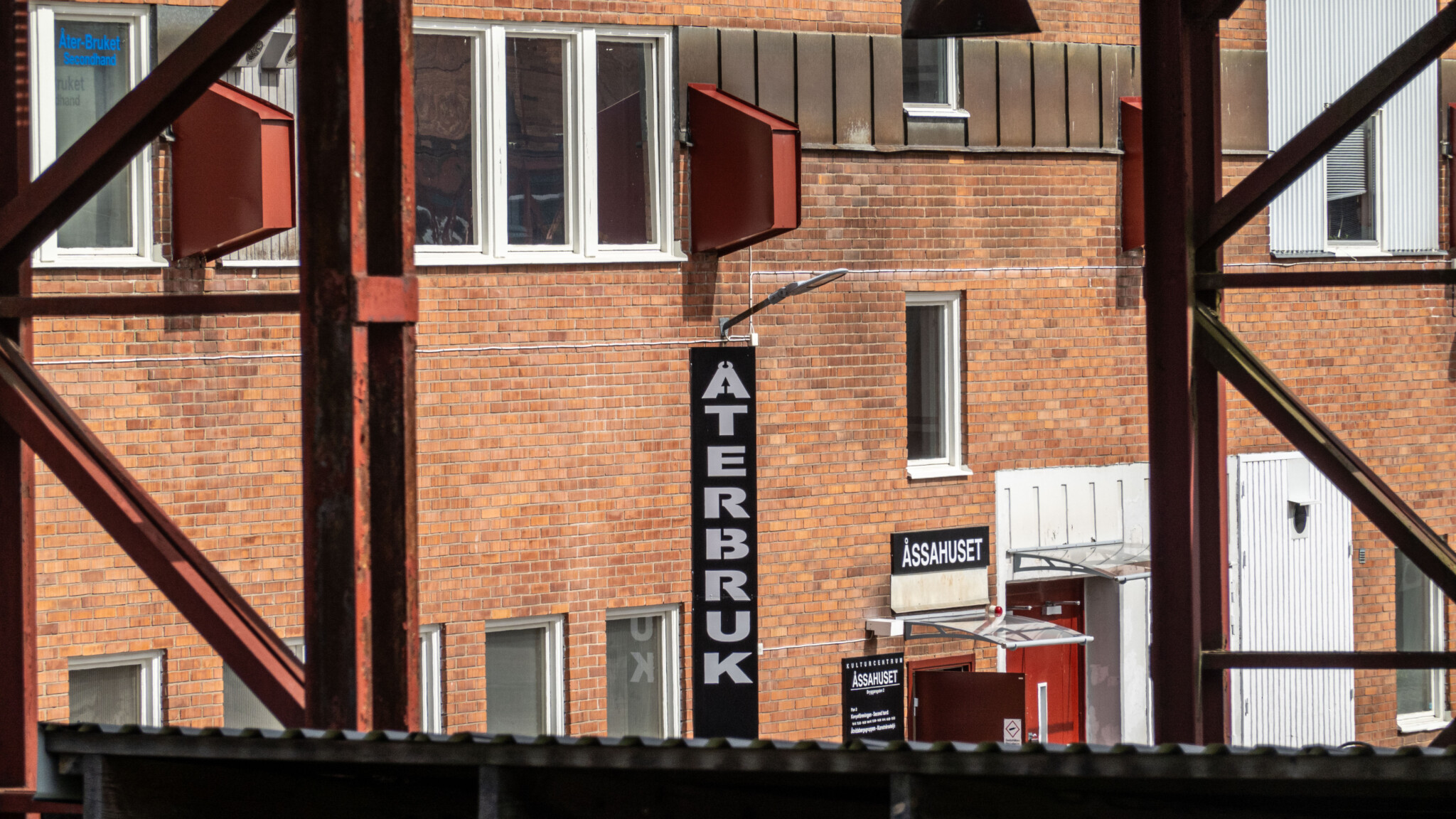 Tegelfasad med skylt för Åter-Bruket secondhand i Åsahuset, Åtvidaberg, sedd genom järnkonstruktioner