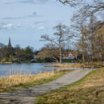 En gångväg slingar sig längs Bysjöns strand med Åtvidabergs kyrka i bakgrunden