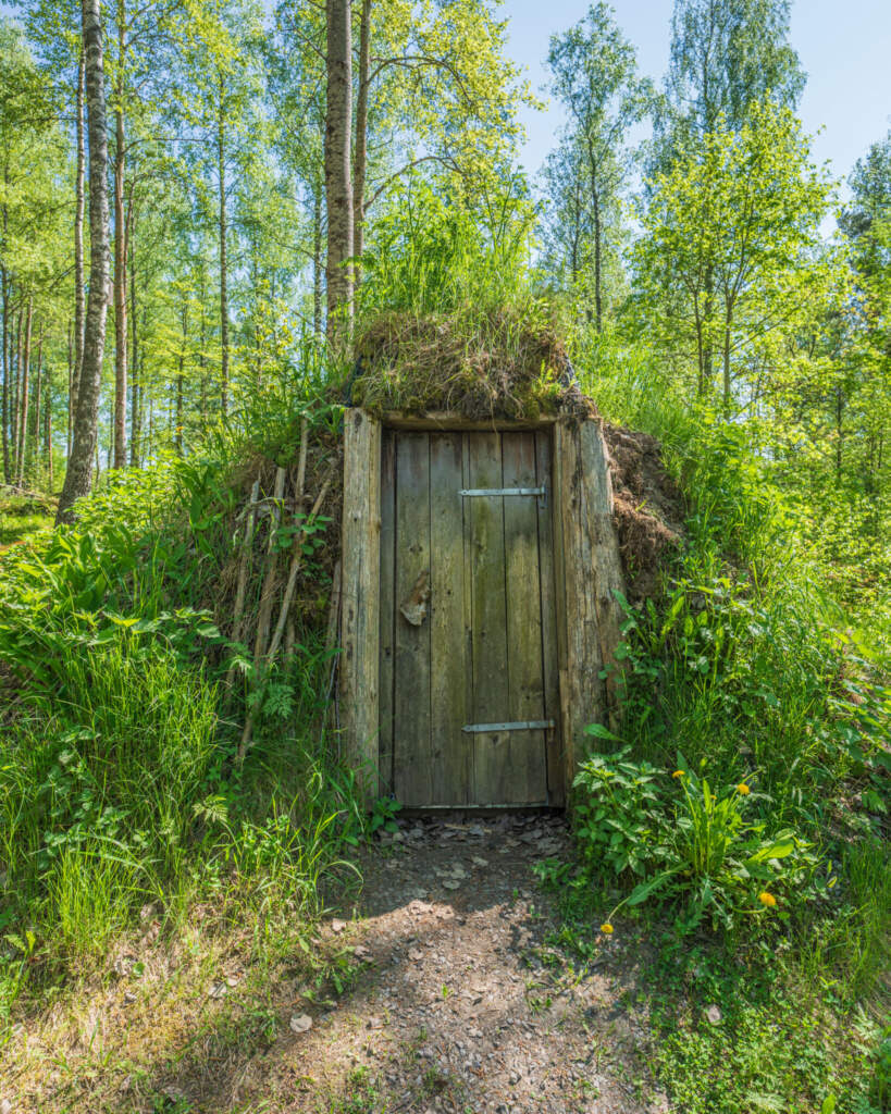 Jordkoja med trädörr och torvtak i grön björkskog vid Magnehults Skogsbruksmuseum i Finspångs kommun, Östergötland