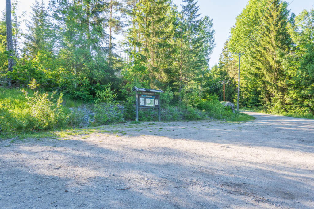 Parkering vid Odensgöl naturreservat med informationstavla, omgiven av barrskog och grönska i sommarljus