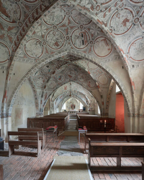 Interiör i S:ta Maria kyrka i Risinge med medeltida kalkmålningar i cirkelmedaljoner på kryssvalven, träbänkar och altare i bakgrunden.