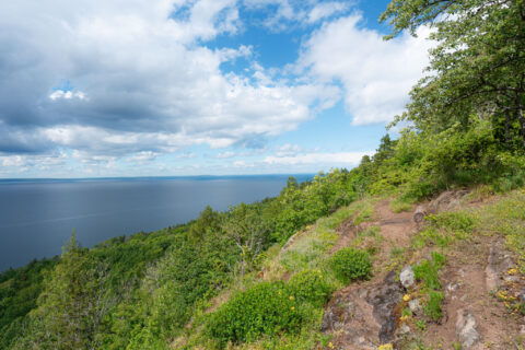 Vandringsled längs Marberget på Omberg med vid utsikt över Vättern en sommardag med dramatiska moln och frodig grönska.