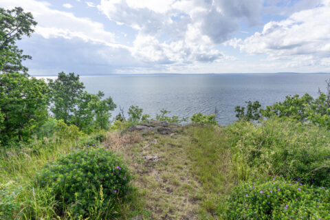 Utsikt över Vättern från Drottning Ommas borg på Omberg, med frodig grönska, klippkant och dramatisk molnhimmel.