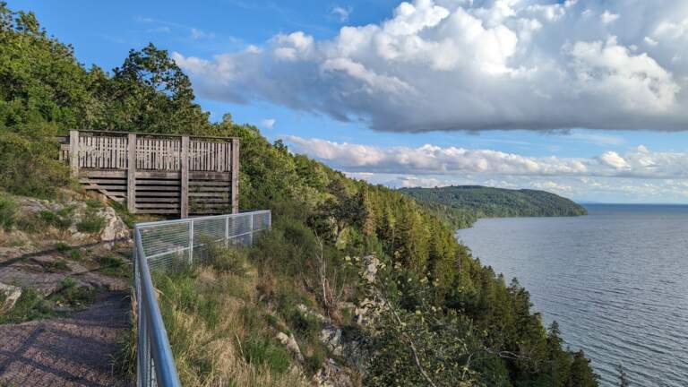 Utsiktsplattform vid Västra väggar på Omberg med panoramavy över Vättern, branta klippor och tät grönskog under molnig himmel.