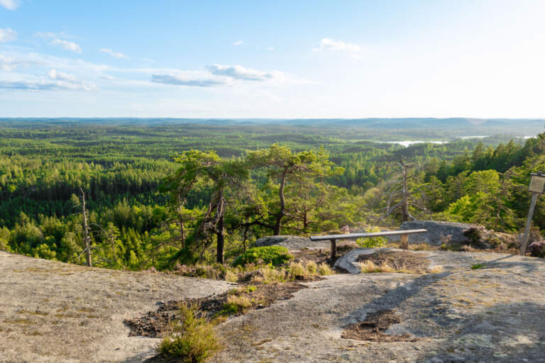 Utsikt från Klevabergets utsiktsplats i Ydre med en bänk på berghällen och vidstäckt vy över grön skog och sjöar i Östergötland