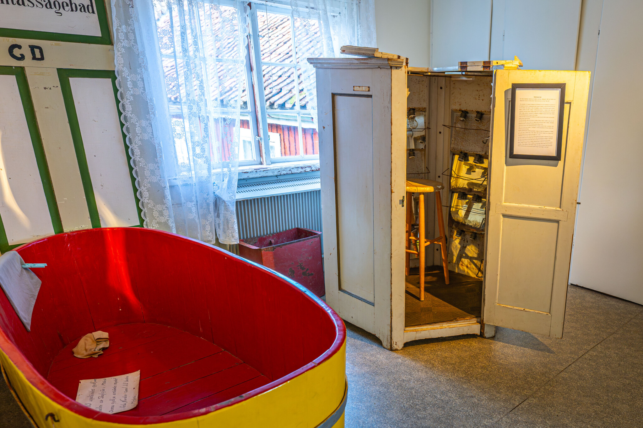Röd och gul badbalja samt öppet vitmålat skåp med medicinsk utrustning på Lazarettsmuséet vid Medevi brunn i Östergötland