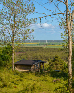 Vindskydd vid Makersbergen på Omberg med vidsträckt utsikt över Östgötaslätten, rapsfält, vindkraftverk och Tåkern i sommargrönska.
