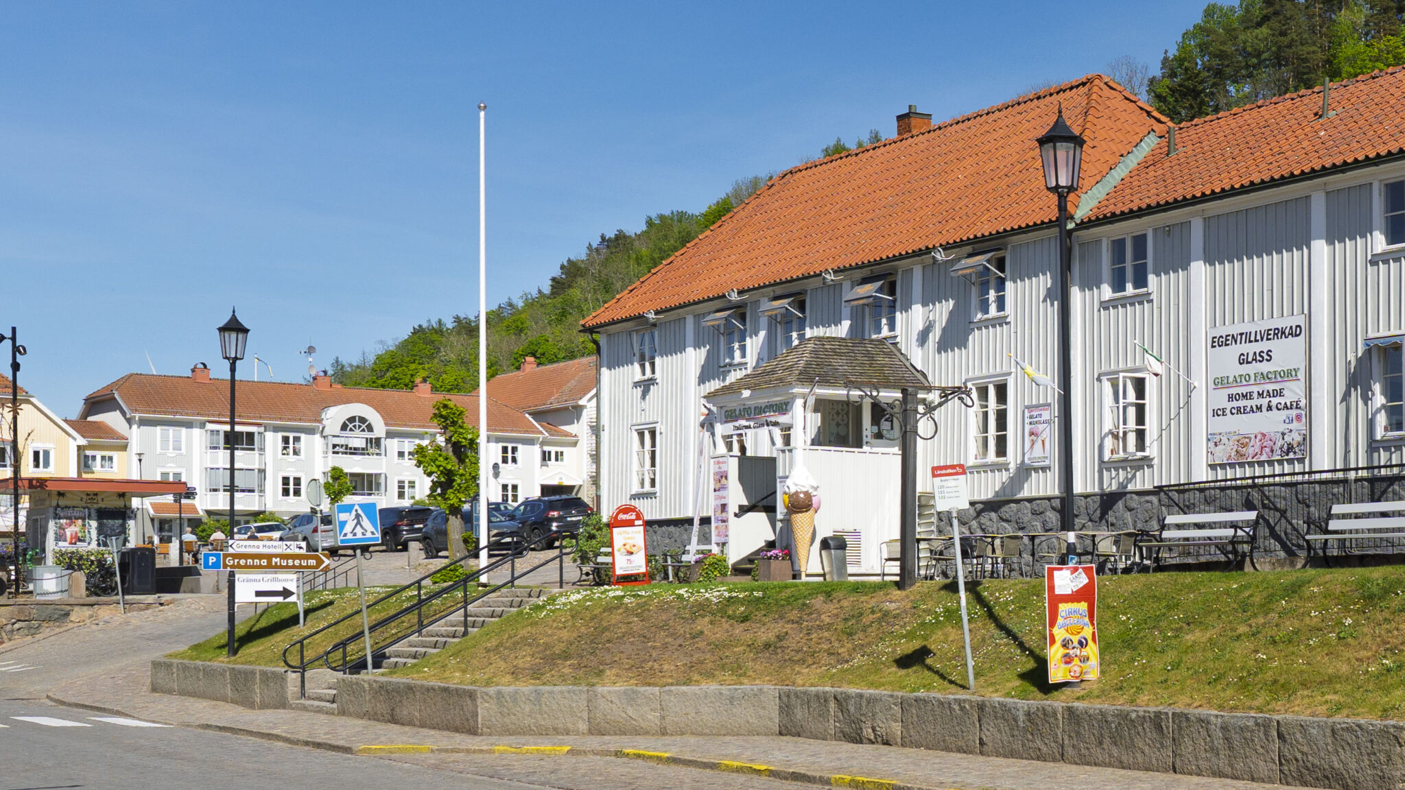 Vita trähus med röda tegeltak i centrala Gränna, med Gelato Factory och skylt för egentillverkad glass, en solig sommardag.