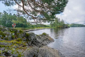Badplats vid Ivägssjön nära Steneby med mossbeklädda klippor, en flytbrygga och en livboj under en tall i Dalsland.