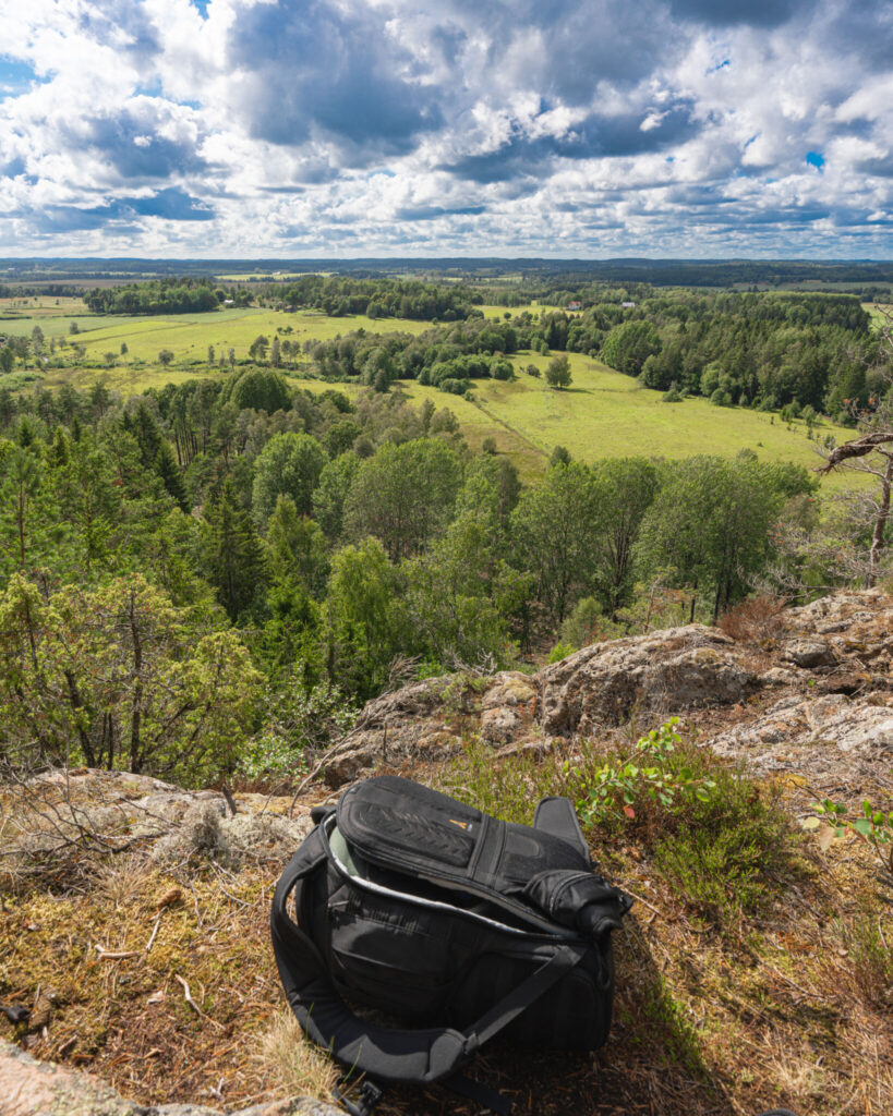 Vidsträckt utsikt över Dalslands gröna ängar och skogar från Nubberudskullen, med en ryggsäck på berghällen i förgrunden
