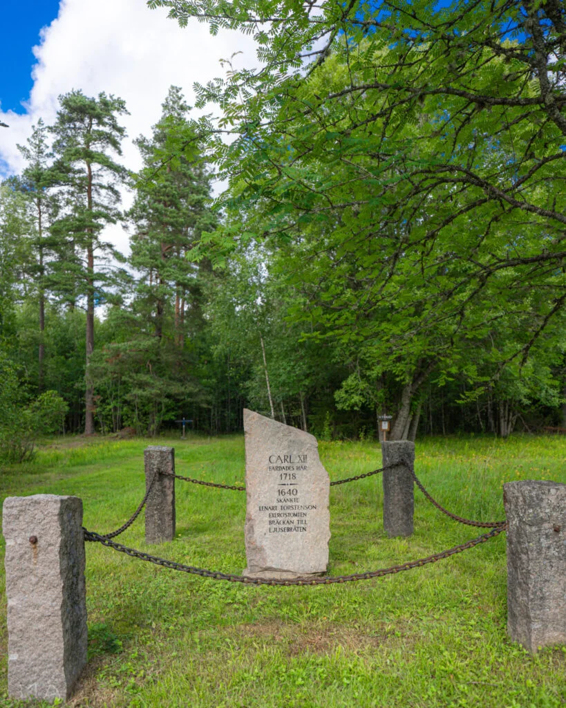 Minnessten över Karl XII:s armé 1718 vid Soldattorpet Bräckan, omgärdad av kedjor och stolpar på en grön gräsmatta i Järbo, Dalsland