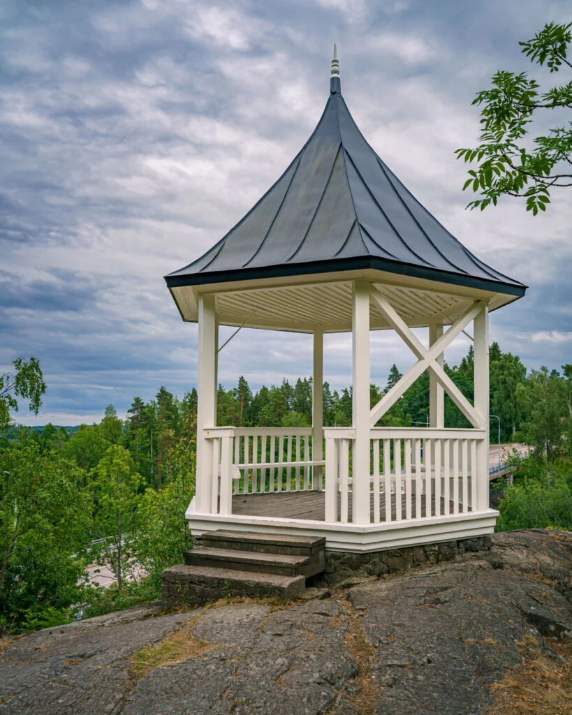 Vit lusthuspaviljong på en klippa i Ramslökedalens naturreservat vid Håverud med utsikt över grön skog och Dalslands kanal.