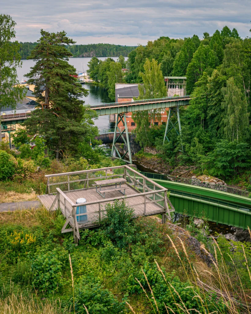 Utsiktsplattform i trä med bänk ovanför Håveruds akvedukt, med gröna järnbroar, forsen och Upperudsälven omgivna av lummig grönska.