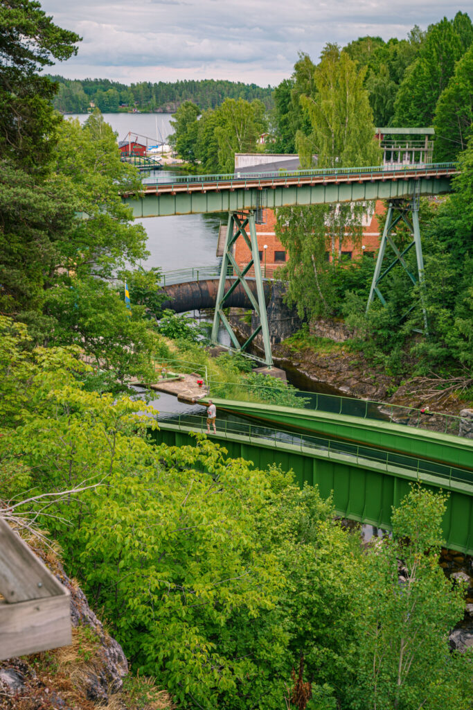 Utsikt över Håveruds akvedukt i Dalsland med två gröna broar, tegelbyggnad och Dalslands kanal omgiven av frodig grönska