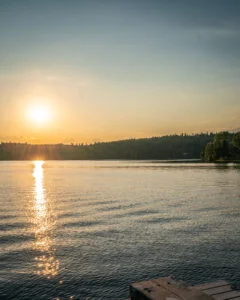 Solnedgång över sjön Råvarpen vid Högsbyn i Tisselskog, Dalsland, med glittrande solreflektion och en badbrygga i förgrunden