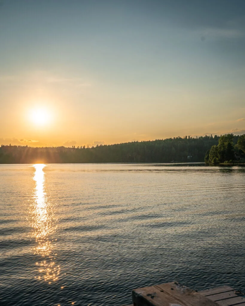 Solnedgång över sjön Råvarpen vid Högsbyn i Tisselskog, Dalsland, med glittrande solreflektion och en badbrygga i förgrunden