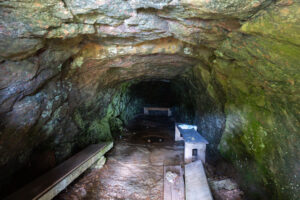 Insidan av eremitgrottan vid Baldersnäs med fuktiga klippväggar, träbänkar och en informationsskylt