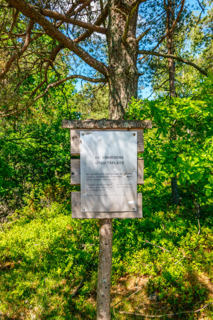 Informationsskylt vid Linhedens utsiktsplats i Dalsland, omgiven av frodig grönska och träd, med text om landskapet mot Vänern