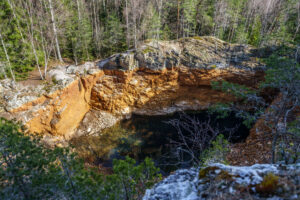 Övergiven gruva vid Bläsen i Fröskog med orange klippväggar och stilla turkost vatten, omgiven av barrskog i Dalsland.