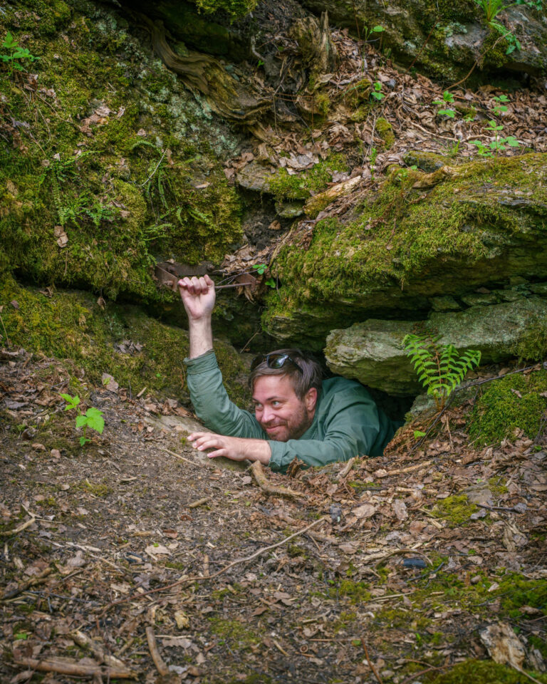 Leende man kryper genom en trång klippöppning kallad Nålsögat längs Doktor Saedéns runda på Kroppefjäll, omgiven av mossiga stenar